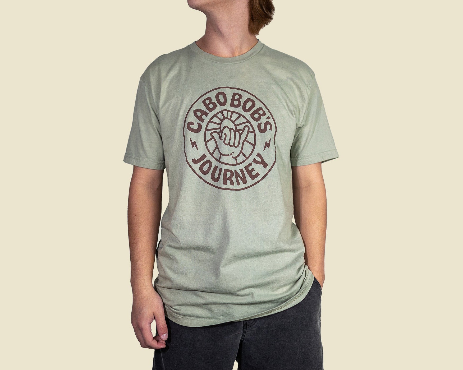 A person wearing a seafoam green t-shirt with 'CABO BOB'S JOURNEY' printed on the front.