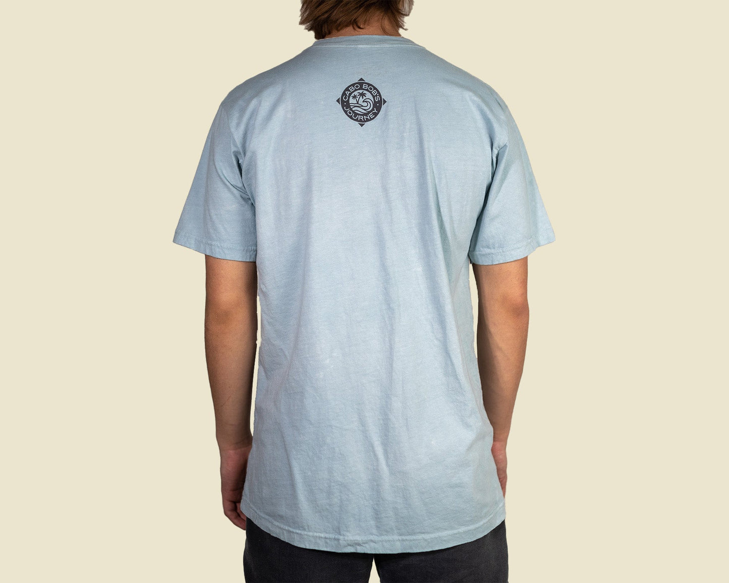 Person wearing a light blue t-shirt with a logo on the back against a beige background