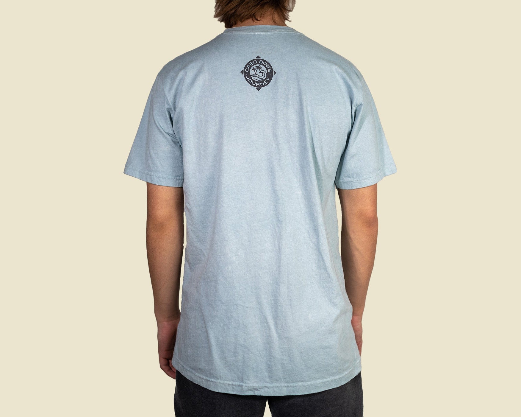 Person wearing a light blue t-shirt with a logo on the back against a beige background